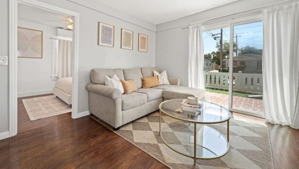 Una sala de estar con un sofá seccional color crema, una mesa de centro de vidrio y vista a un jardín trasero a través de puertas correderas de cristal.