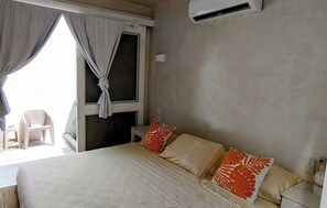 Une chambre à coucher avec un lit, des oreillers, une fenêtre avec des rideaux, une chaise et un appareil de climatisation.