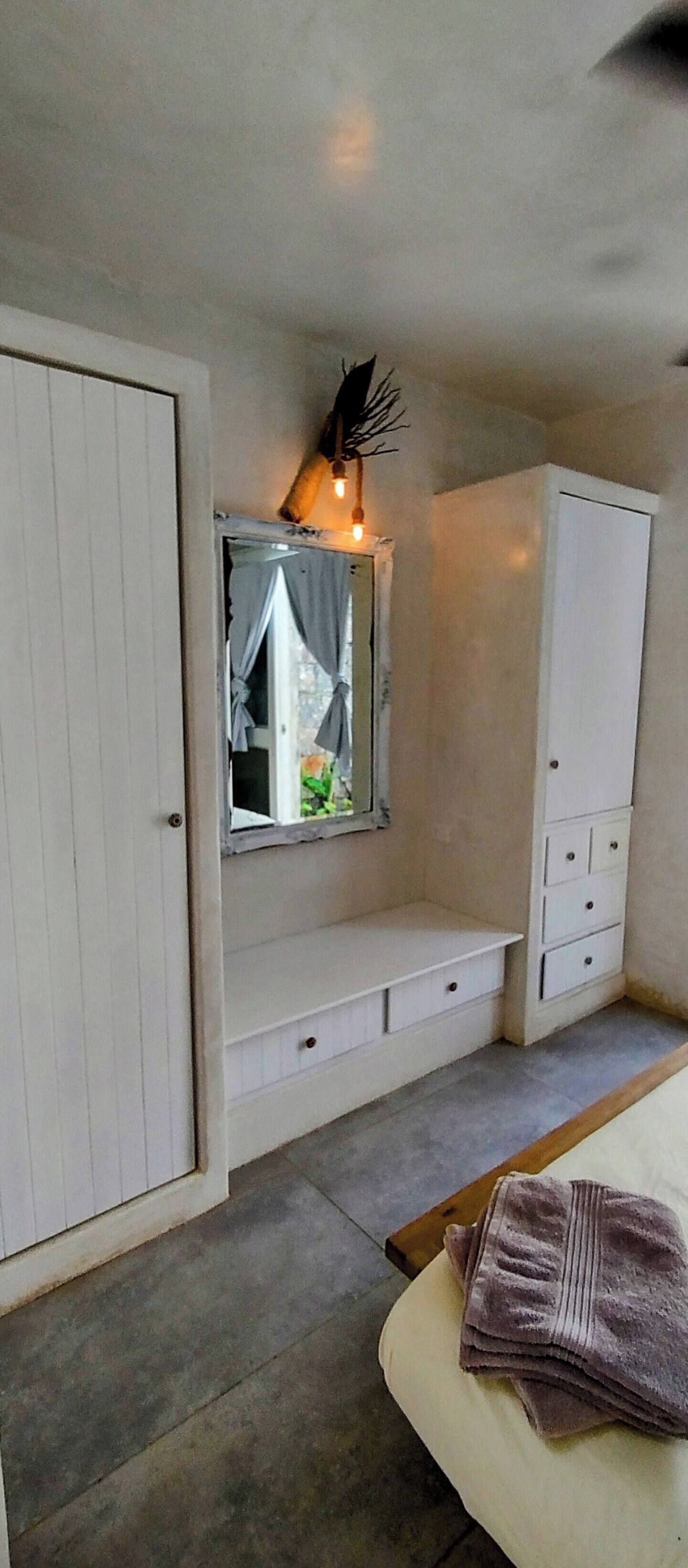 Ein Schlafzimmer mit Bett, Kleiderschrank, Spiegel und einer kleinen Bank.