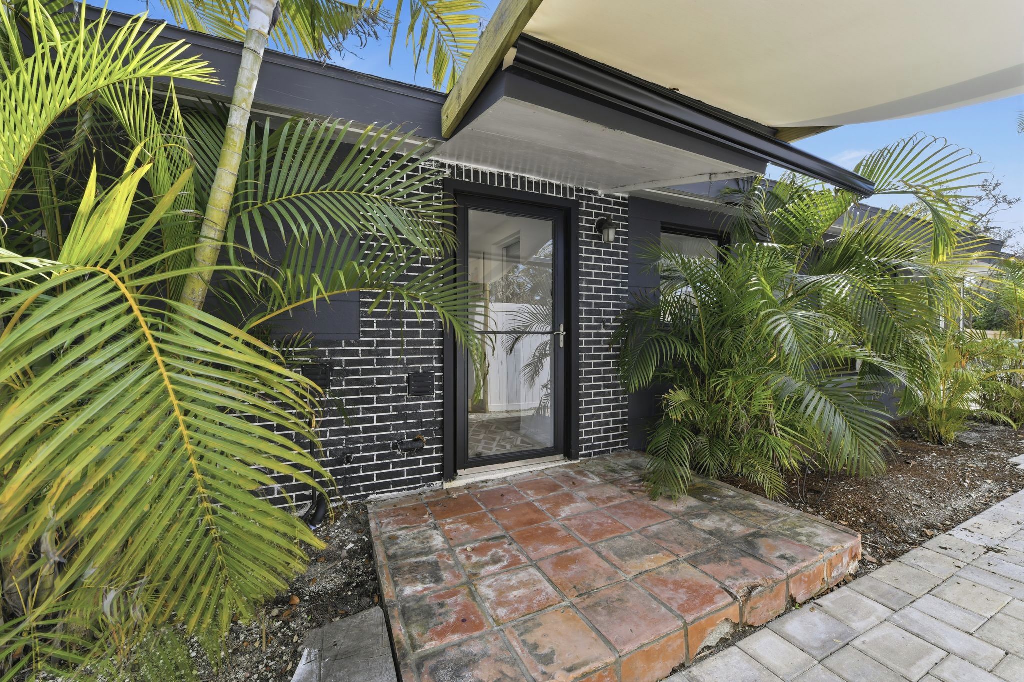 A modern building with a brick facade, a glass door entrance, and a paved pathway leading to the door.