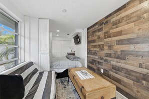 A compact room with a sofa, a bed, a wooden accent wall, and a television mounted on the wall.