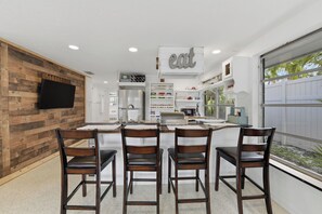 A modern kitchen with a central island, wooden wall paneling, and a flat-screen TV mounted on the wall.