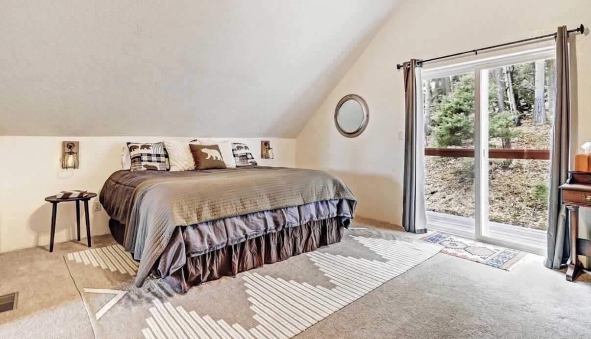Une chambre à coucher avec un grand lit, une table de chevet, un miroir et une porte-fenêtre coulissante donnant sur un balcon.
