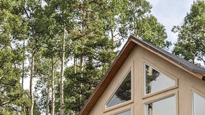 A modern two-story house with a balcony, surrounded by tall trees.