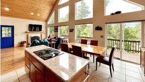 A spacious kitchen with a large island, wooden ceiling, and large windows offering views of the outdoors.
