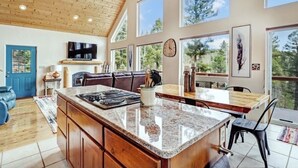 A spacious kitchen with a large island, wooden cabinets, and a view of the outdoors through large windows.