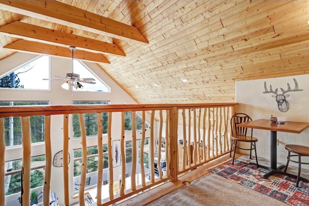 Un balcon en bois avec une balustrade, une table avec des chaises et un mur orné d’une illustration de cerf.