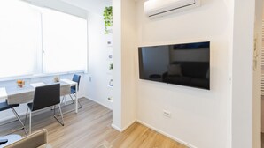 Een moderne kamer met een flatscreen televisie aan de muur, een eettafel met stoelen en een raam met blinds.