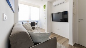 Een moderne woonkamer met een bank, televisie en een eethoek op de achtergrond.