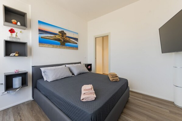 A modern bedroom with a bed, a painting, a TV, and a door.