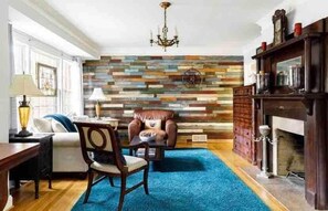 A living room with a blue carpet, a fireplace, a wooden wall, and a chandelier.