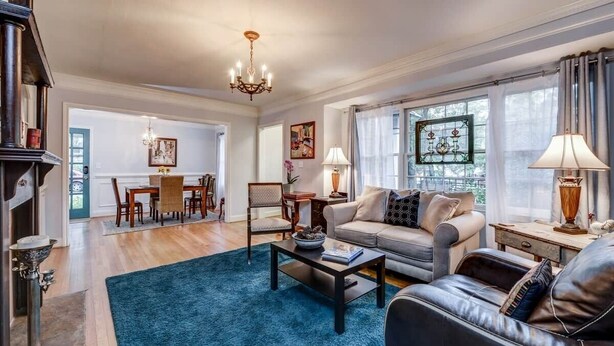 A living room with a sofa, coffee table, and a chandelier. There is a dining area with a table and chairs. - Atlanta Llama Luxury Cottage (Atlanta)