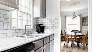 A kitchen with white subway tiles, a dishwasher, a coffee maker, and a dining area with a table and chairs. - Atlanta Llama Luxury Cottage (Atlanta)