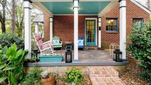 A covered porch with brick walls, outdoor furniture, and potted plants. - Atlanta Llama Luxury Cottage (Atlanta)