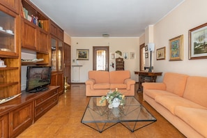 A living room with a sofa, a glass coffee table with a vase, wooden cabinets, and a television.