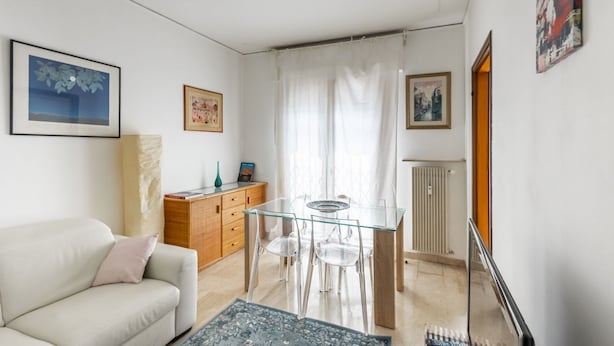 Una sala de estar con un sofá, una mesa de comedor de vidrio y sillas, un mueble de madera y un radiador.