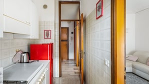 Una cocina con armarios blancos, un refrigerador rojo y piso de baldosas.