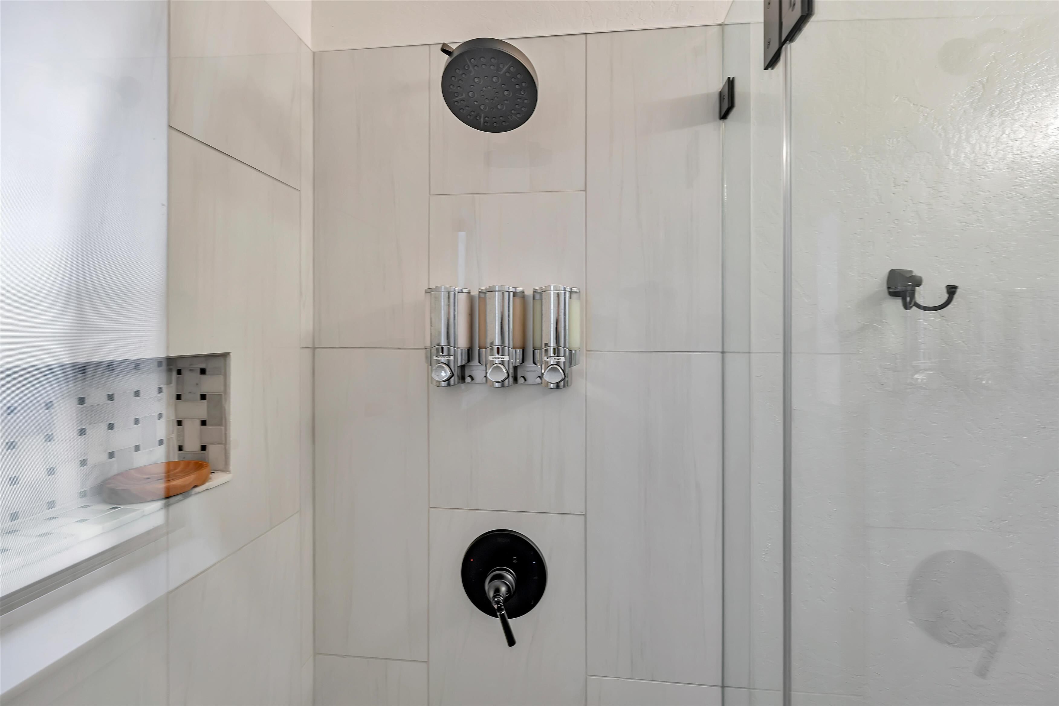 A modern bathroom with a glass shower enclosure, a toilet, and a sink with a soap dispenser.