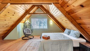A cozy attic bedroom with a sloped wooden ceiling, a bed with a quilt, a rocking chair, and a window with blinds. - Lakeside Retreat: Newly Renovated Home with lake views and Hot tub (Groveland)