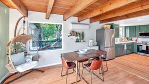 A modern kitchen with wooden beams, a dining area with a swing chair, and a view of greenery outside. - Lakeside Retreat: Newly Renovated Home with lake views and Hot tub (Groveland)