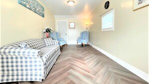 Una camera d'albergo con pavimento in legno a motivi a spina di pesce, un letto con copripiumino a quadri, due poltrone blu e una porta che conduce a un'altra stanza.