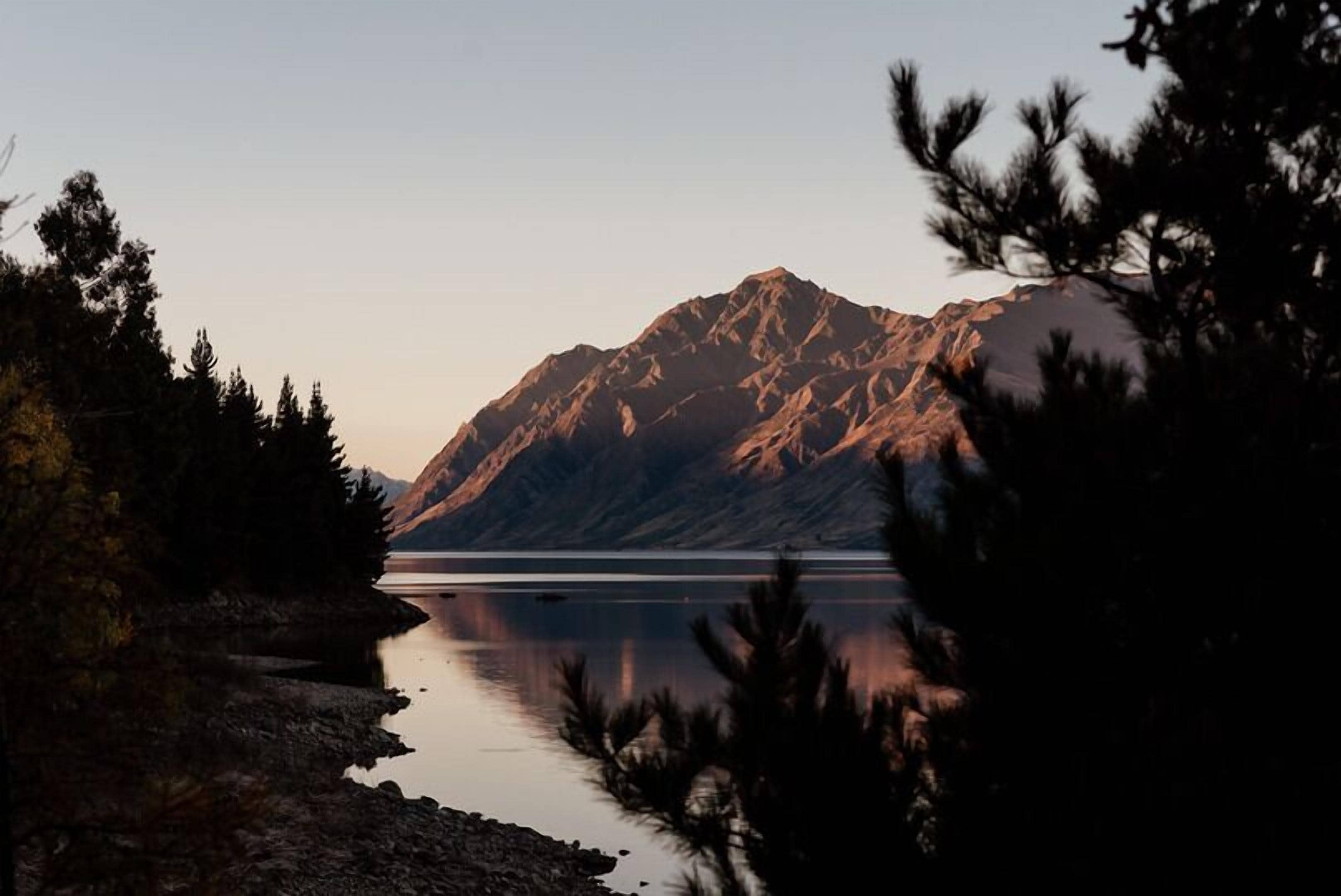A mountain landscape with a calm lake and forested area.