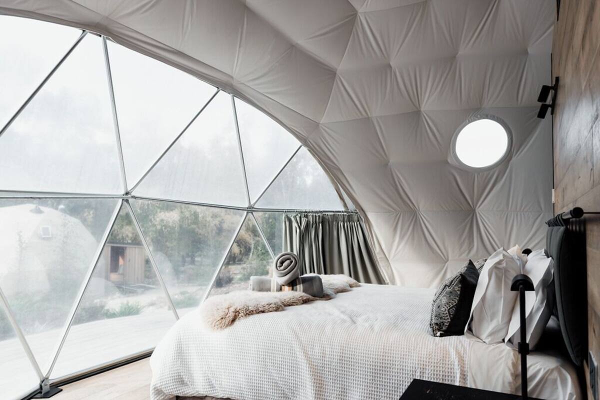 Ein Zelttraum mit Bett, einem runden Dachfenster und Blick ins Freie.
