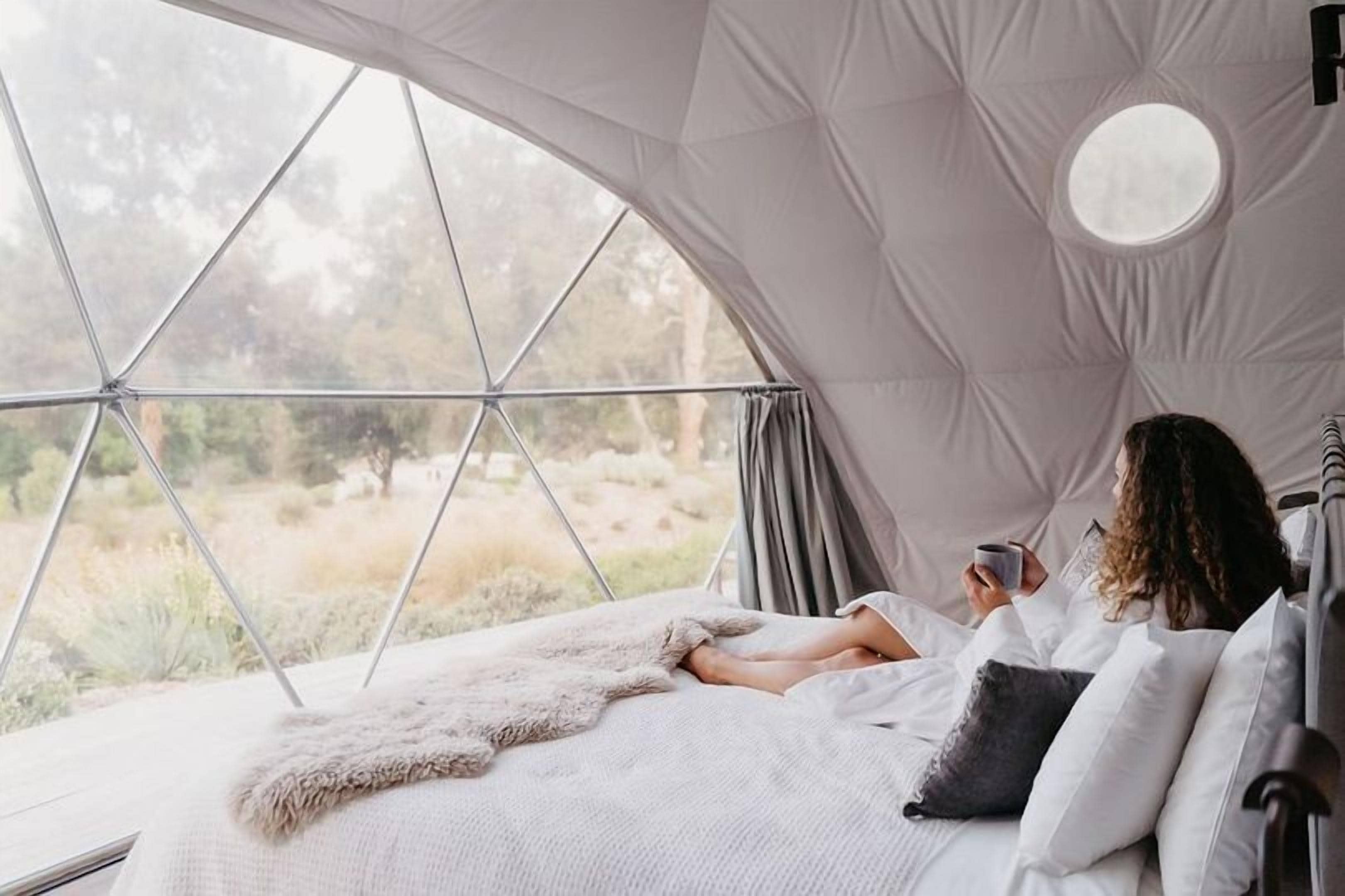 Interior acogedor de una cúpula geodésica con una cama, una manta de piel y vistas al exterior.