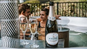 A bottle of Maude champagne and two glasses on a table outdoors. - Cross Hill Glamping (Lake Hawea)