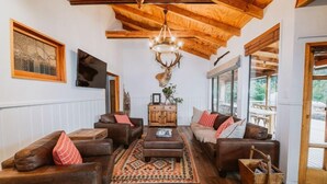 A cozy living room with leather sofas, a wooden coffee table, and a large deer head mounted on the wall. - Cross Hill Glamping (Lake Hawea)