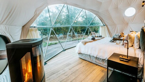 A cozy tented room with a bed, a heater, and a view of the outdoors. - Cross Hill Glamping (Lake Hawea)