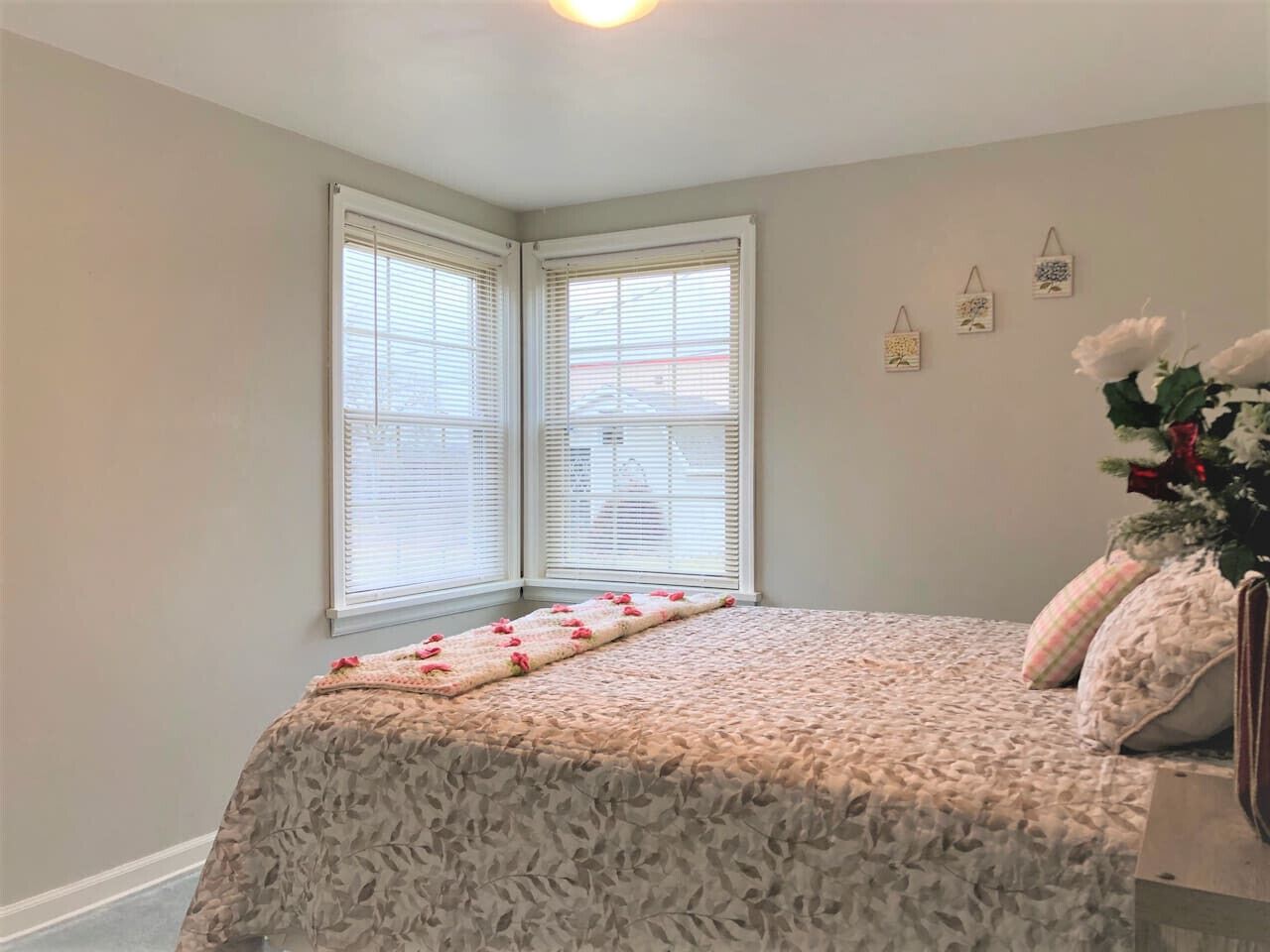 A bedroom with a bed, a window with blinds, and a wall with three small decorative items.
