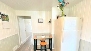 A narrow hallway with a wooden table and two stools, a white refrigerator, and a door at the end. - North - Family Neighborhood, Pet Friendly (Paulding)