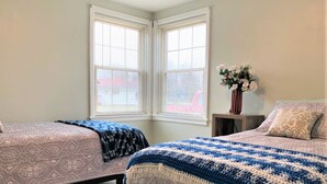 A bedroom with two beds, a window with blinds, a nightstand with a vase of flowers, and a patterned rug. - North - Family Neighborhood, Pet Friendly (Paulding)