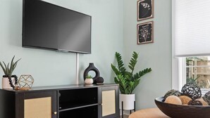 Uma sala de estar moderna com um móvel de entretenimento preto, uma televisão de tela plana e plantas decorativas.