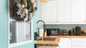 Uma cozinha com armários brancos, bancada de madeira, pia, micro-ondas, cafeteira e uma grinalda decorativa na parede.