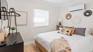 Quarto com cama, mesa de cabeceira, luminária, decoração na parede e ar condicionado.