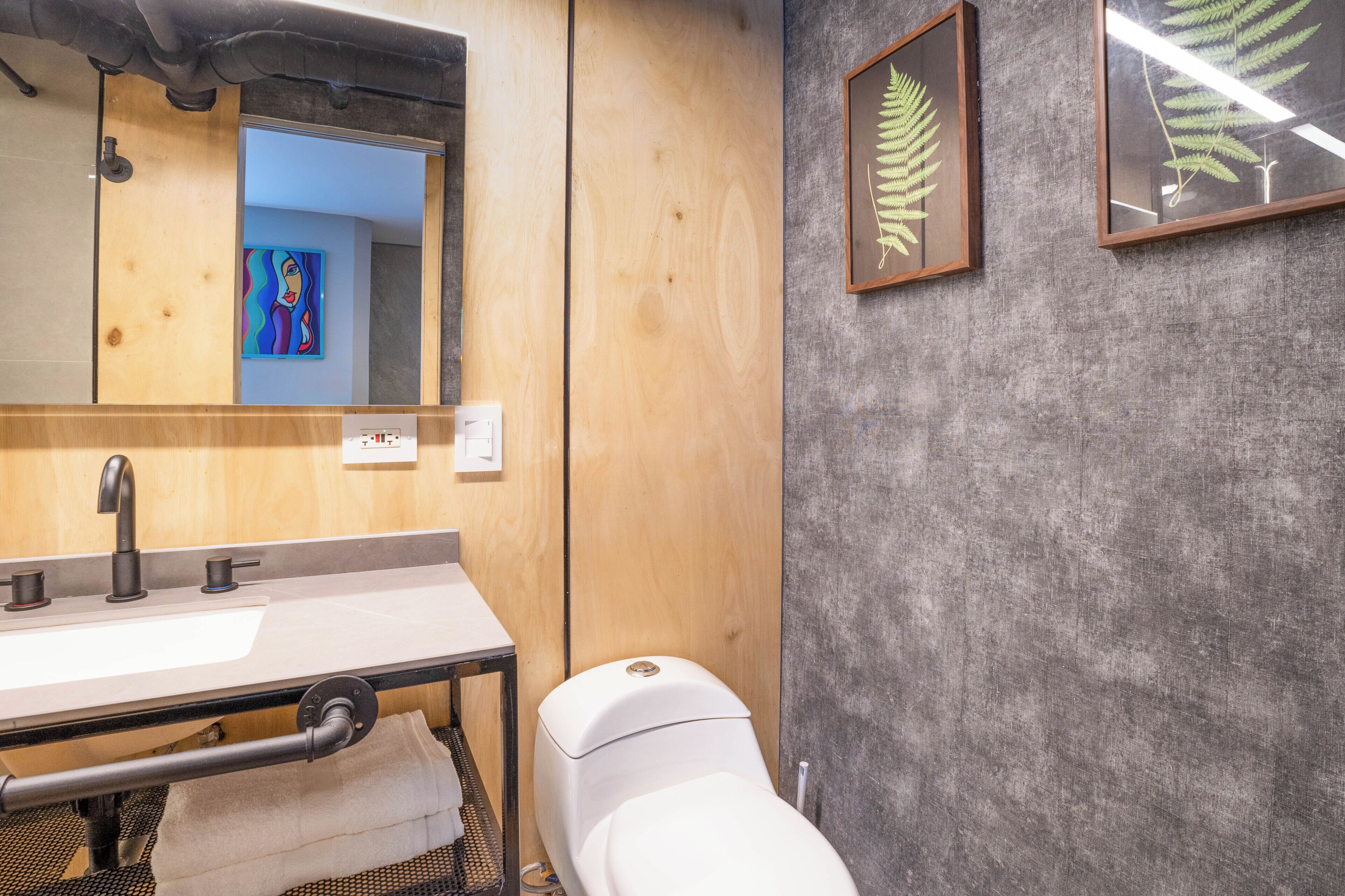 A bathroom with a wooden vanity, a white toilet, a mirror, and framed botanical prints on the wall.