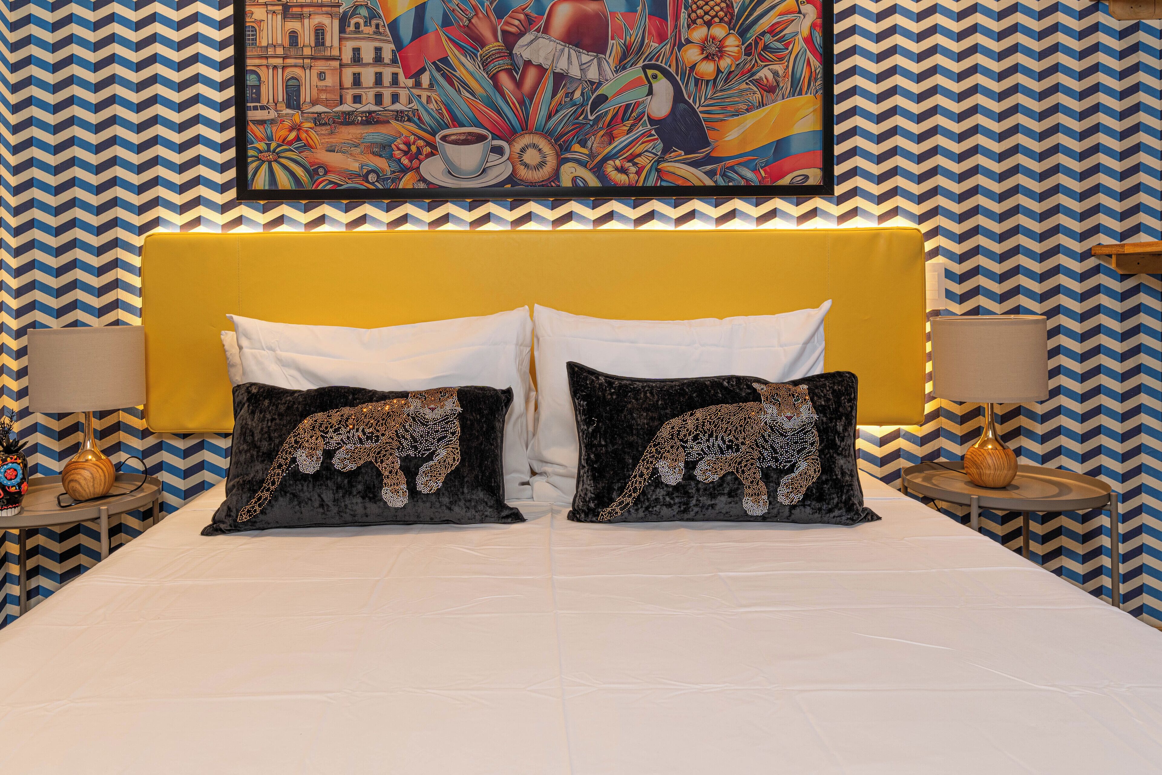 A bed with two black pillows featuring a leopard design, a yellow headboard, and a colorful mural on the wall behind.