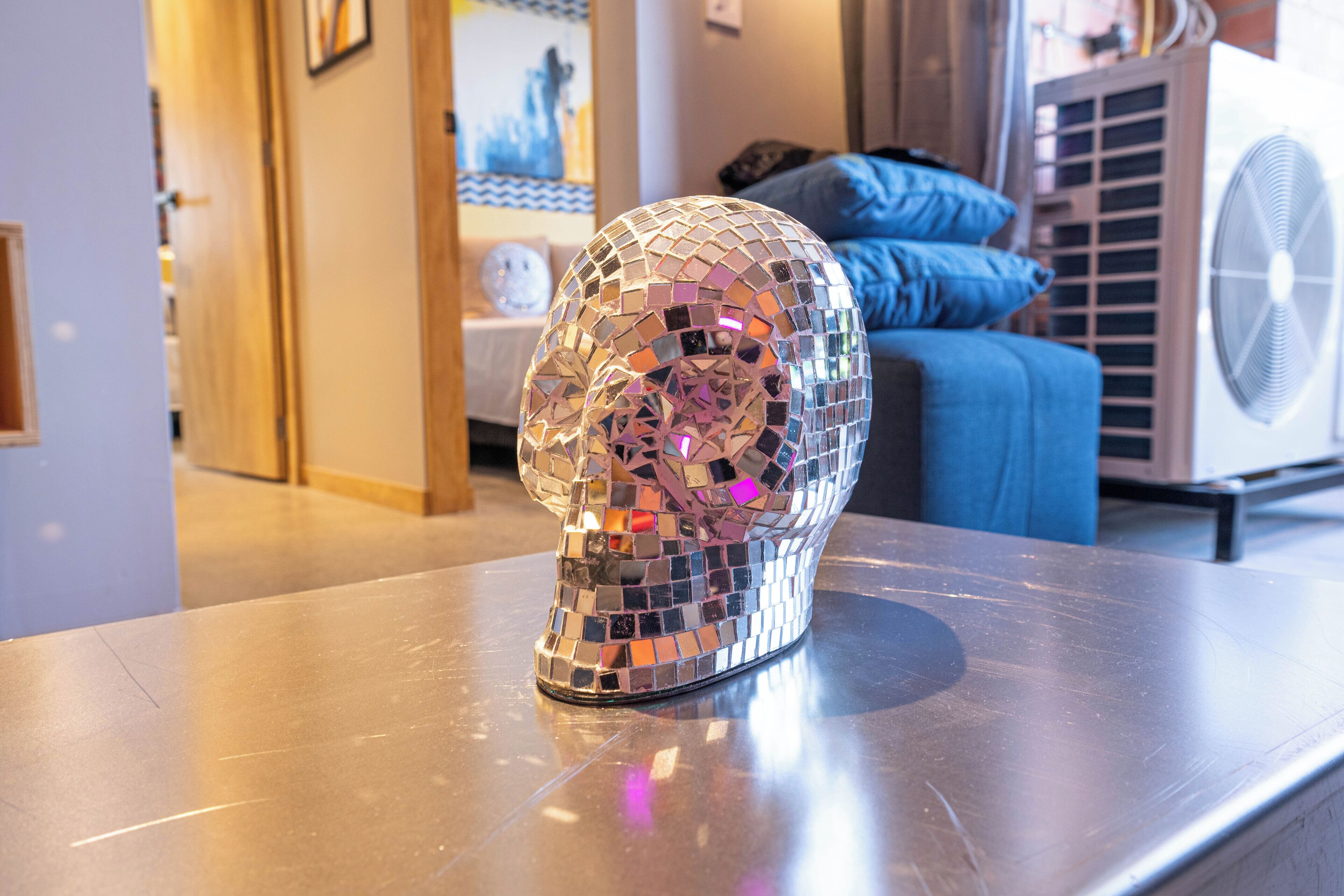 A room with a metallic table, a decorative skull sculpture, a blue sofa, and a white fan.