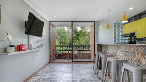 A modern kitchen with yellow cabinets, a flat-screen TV, and a balcony with chairs.