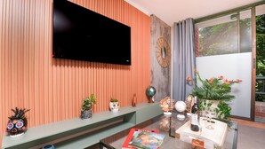 A modern living room with a flat-screen TV mounted on a wooden wall, a glass coffee table with a magazine, a small plant, and a decorative globe.