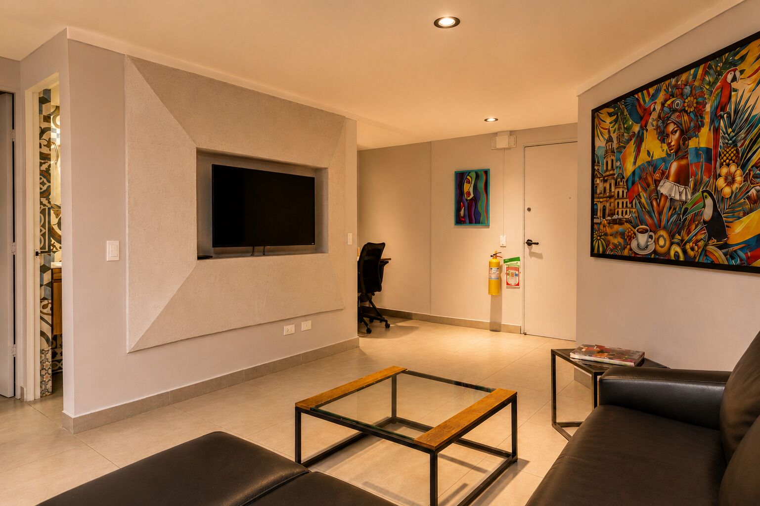 Un salon moderne avec un téléviseur à écran plat, une table basse en verre, un canapé et un tableau abstrait aux couleurs vives accroché au mur.