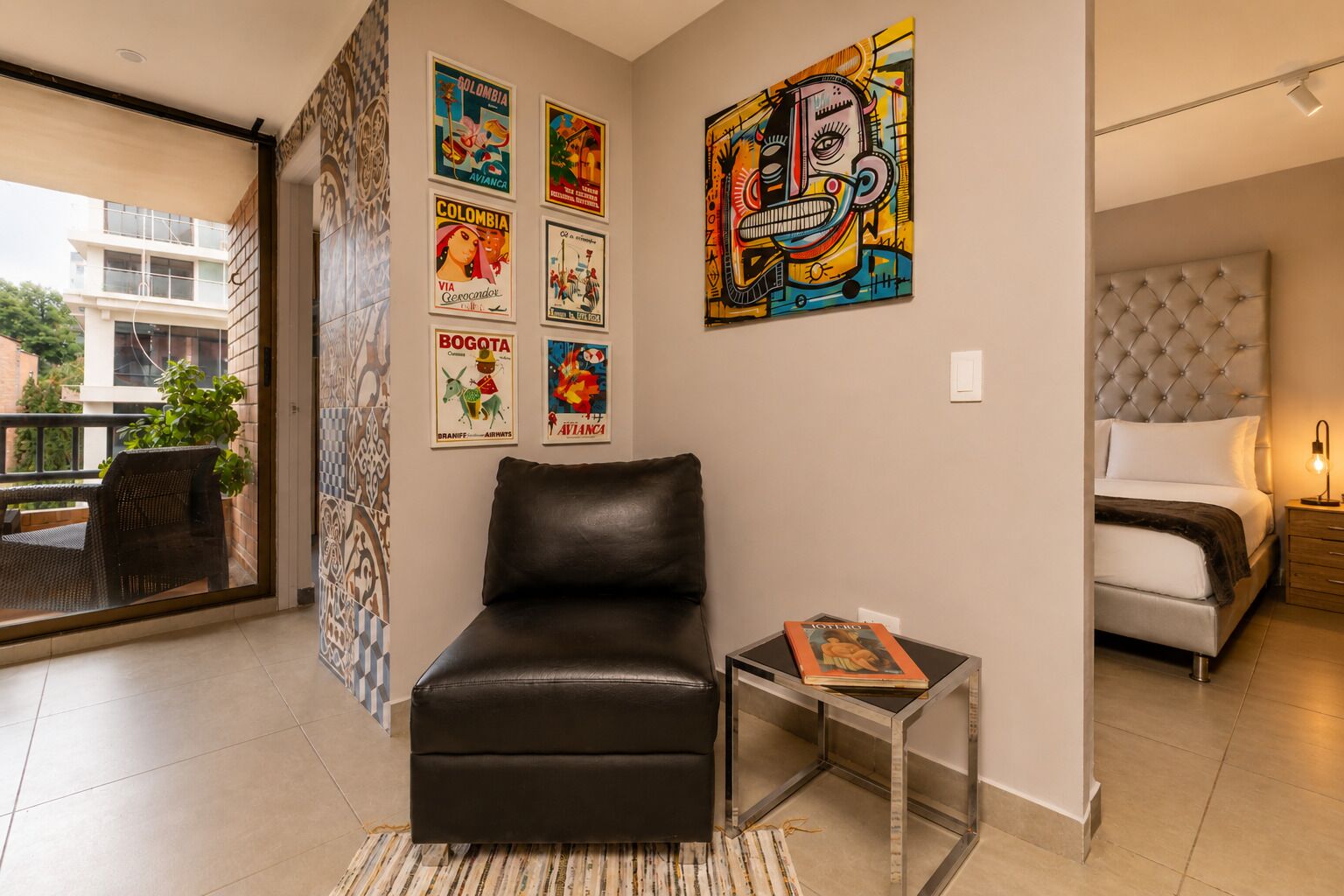 Una sala moderna con un sofá de cuero, una mesa de centro de vidrio y una cama con cabecera capitonada.