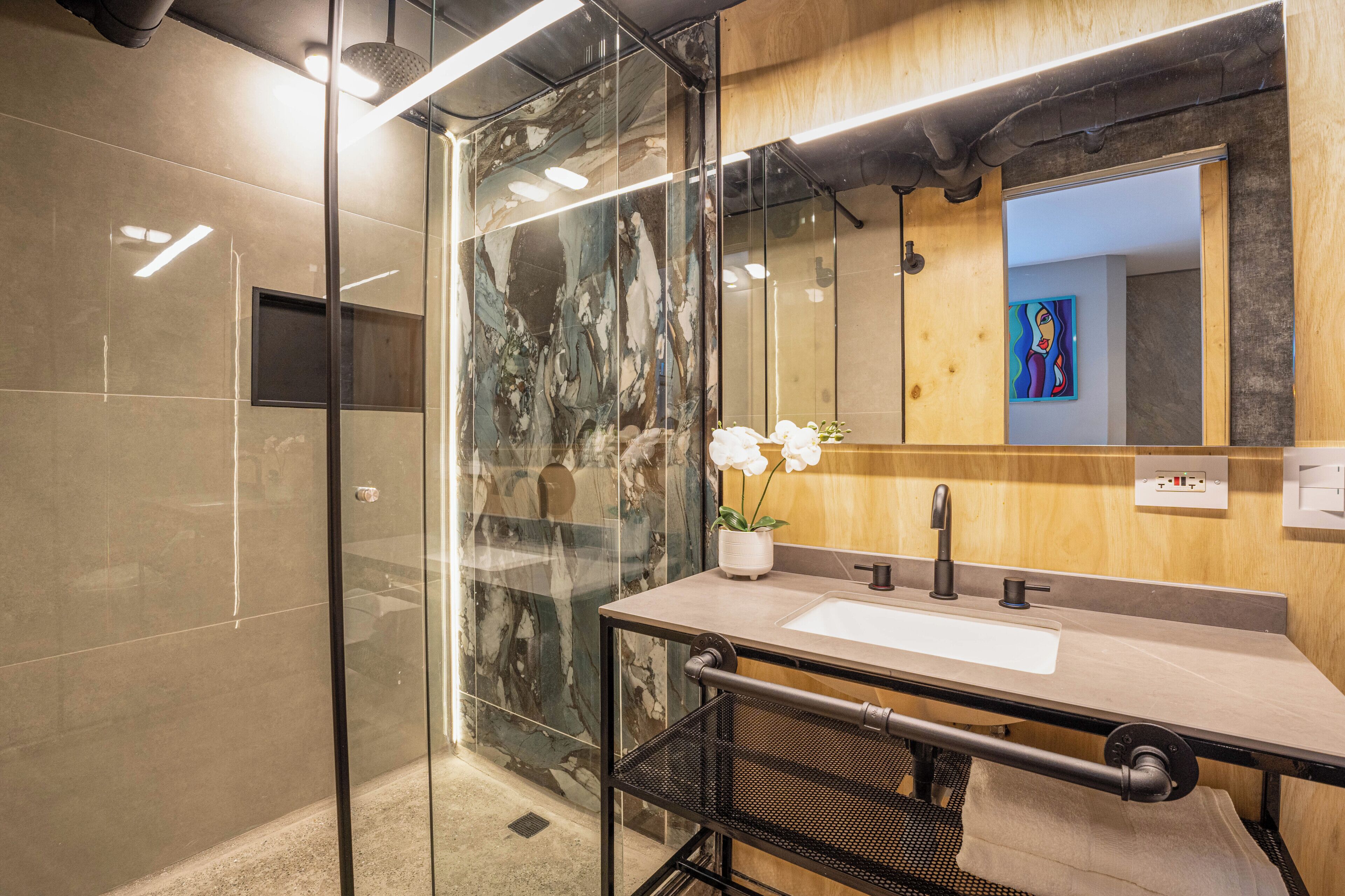 A modern bathroom with a glass shower enclosure, a marble backsplash, a sink with a black faucet, and a potted orchid.