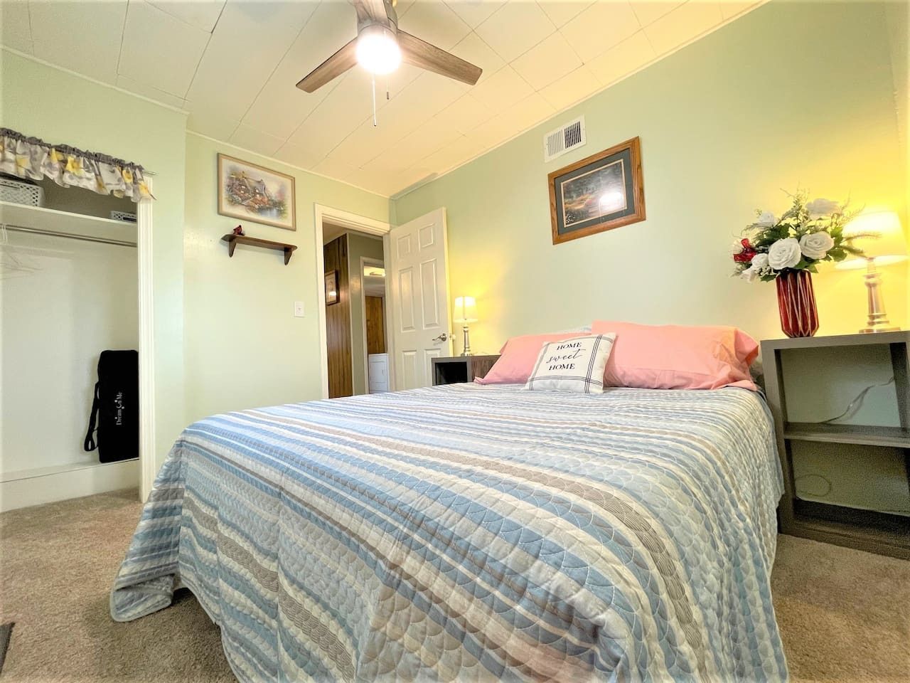 A bedroom with a bed, a ceiling fan, a nightstand, a lamp, and a wall-mounted shelf.