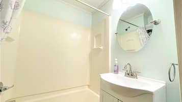 A bathroom with a bathtub, a sink with a mirror, and a shower curtain.