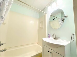 Une salle de bain avec une baignoire, un lavabo avec un miroir et un rideau de douche.