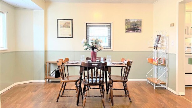 Un comedor con una mesa y sillas de madera, un florero con flores, cuadros en la pared y una ventana con persianas.