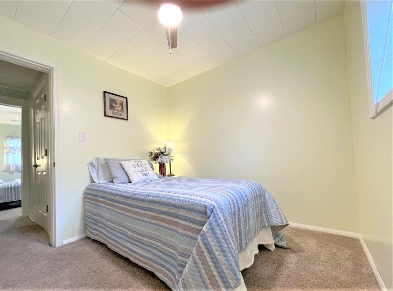 A bedroom with a bed, a nightstand, a framed picture on the wall, and a door leading to another room.